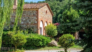 A stone building with a tiled roof, surrounded by lush greenery and trees. - Agr. Lampugnano (Civitella Paganico)