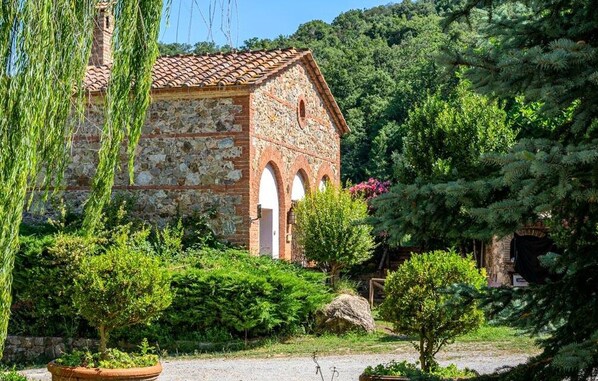 Un edificio de piedra con tejado de baldosas, rodeado de exuberante vegetación y árboles.