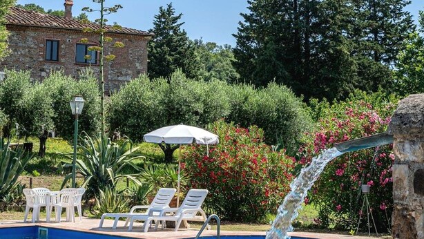 A pool area with lounge chairs, a stone building, and lush greenery. - Agr. Lampugnano (Civitella Paganico)