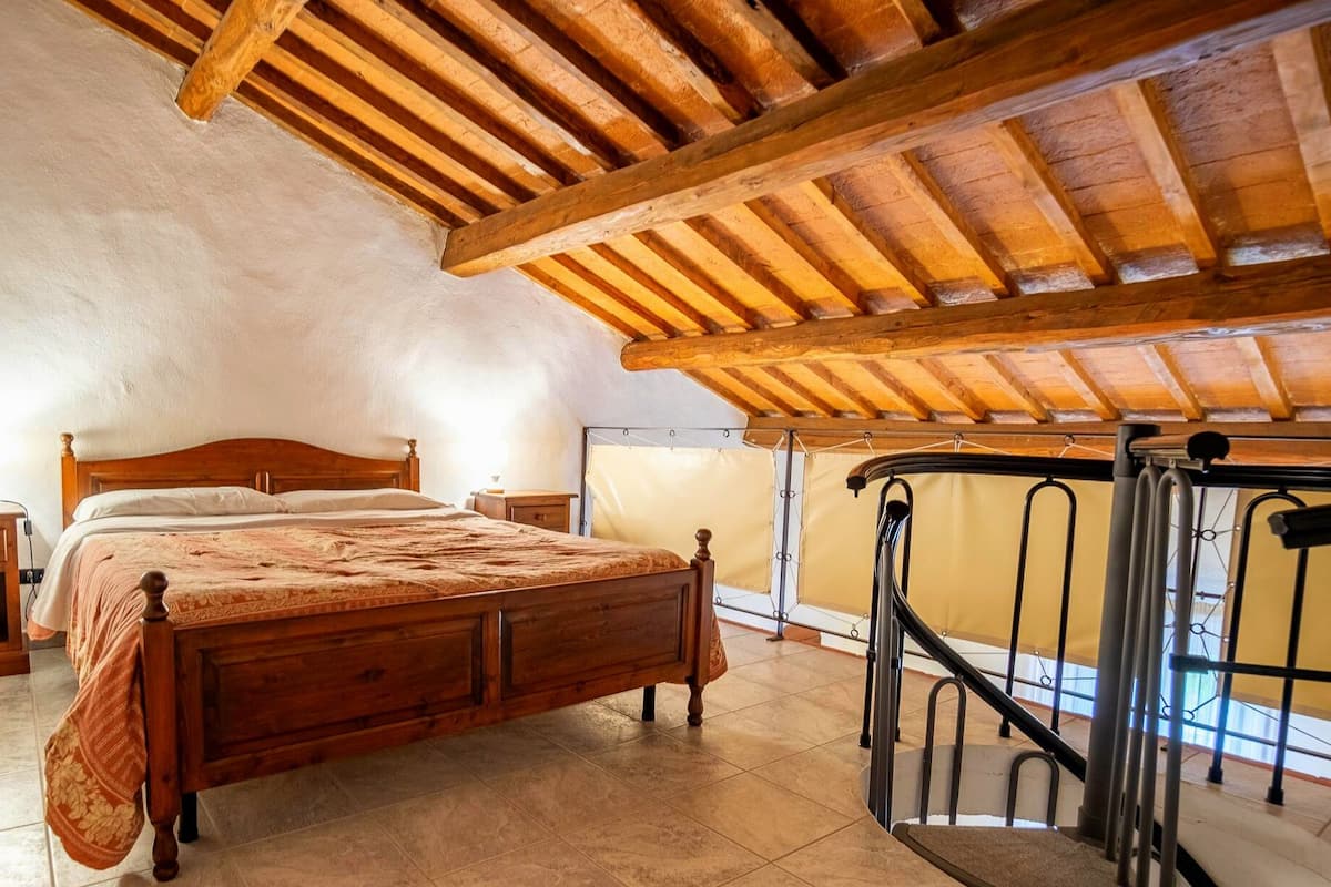 Ein Schlafzimmer mit einem hölzernen Bett, einem Nachttisch, einem Fenster mit Blick und einer Treppe.