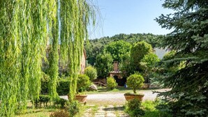A garden with a variety of trees and shrubs, a stone pathway, and a rustic building in the background. - Agr. Lampugnano (Civitella Paganico)