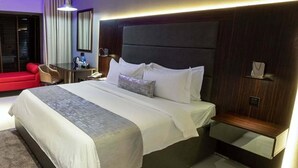 Une chambre d’hôtel moderne avec un grand lit, une table de chevet, un fauteuil rouge, un bureau et un miroir.