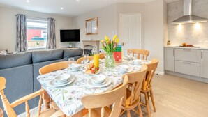 A modern living room with a sofa, dining table set for four, and a kitchen area with cabinets and a stove.