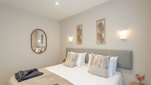 A neatly made bed with a grey headboard, a round mirror, and two wall-mounted light fixtures.