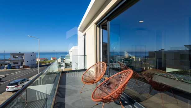 A balcony with two orange chairs, a glass railing, and a view of the sea and buildings. - Casa Mango by Acasadascasas (Mafra)