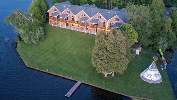 A large, multi-story lodge with a dock and a teepee on a grassy island. - #5 Lakefront Hamlin Lake Retreat - Sleeps 10 (Ludington)