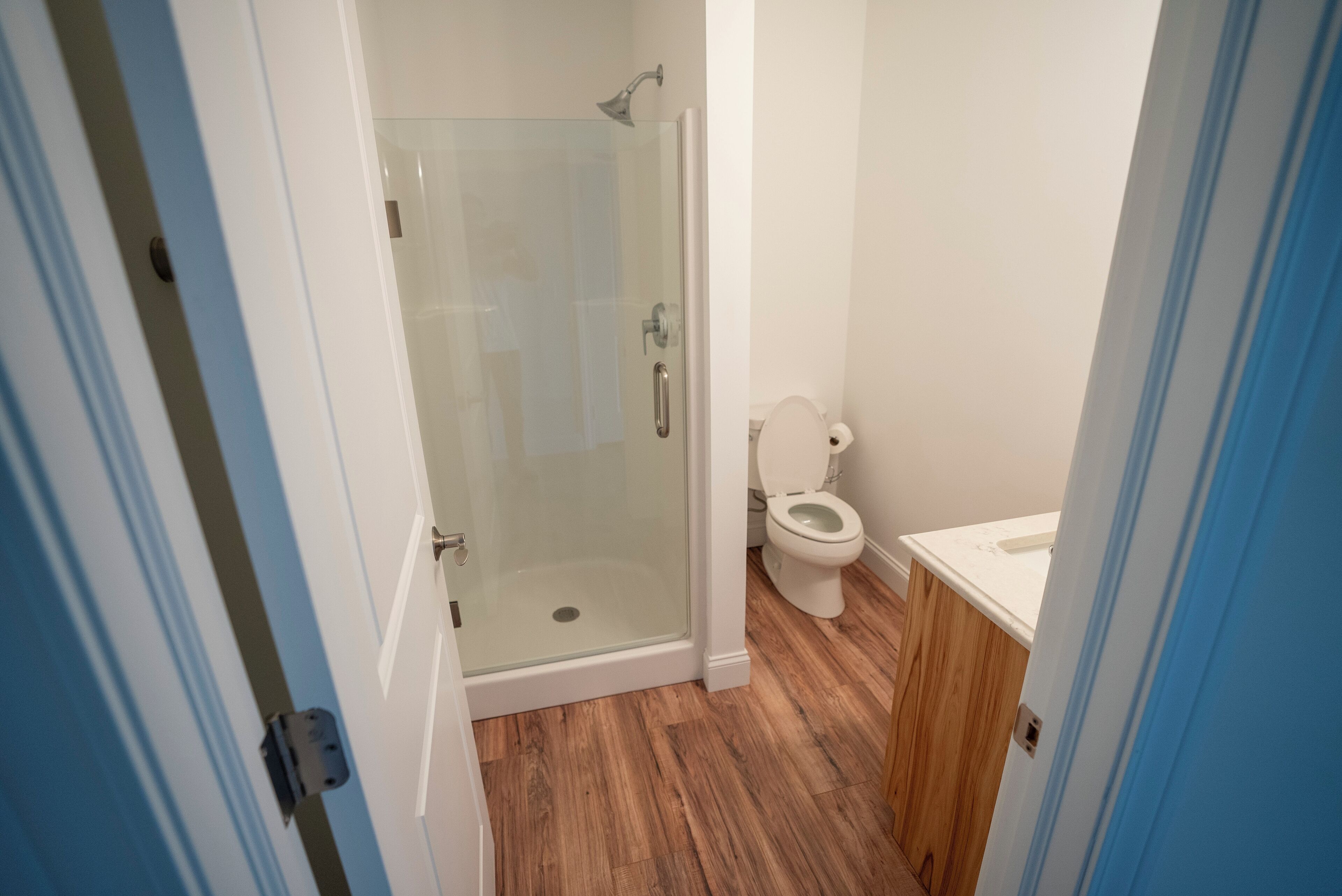 Un baño con ducha envuelta en vidrio, inodoro y suelo de madera.