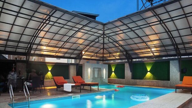 Piscina interna com teto de vidro, cadeiras de descanso e área de bar.
