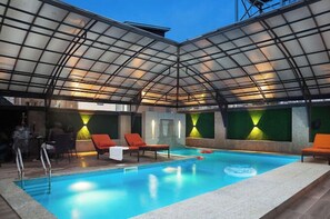 An indoor swimming pool with a glass ceiling, lounge chairs, and a bar area. - Phoenix Imperial Hotel and Apartment (Abuja)