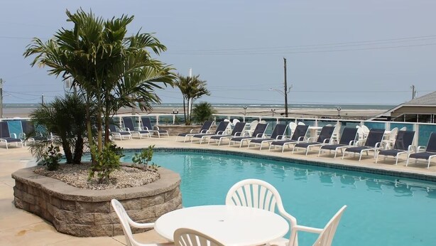 A pool area with lounge chairs and a table, surrounded by palm trees.