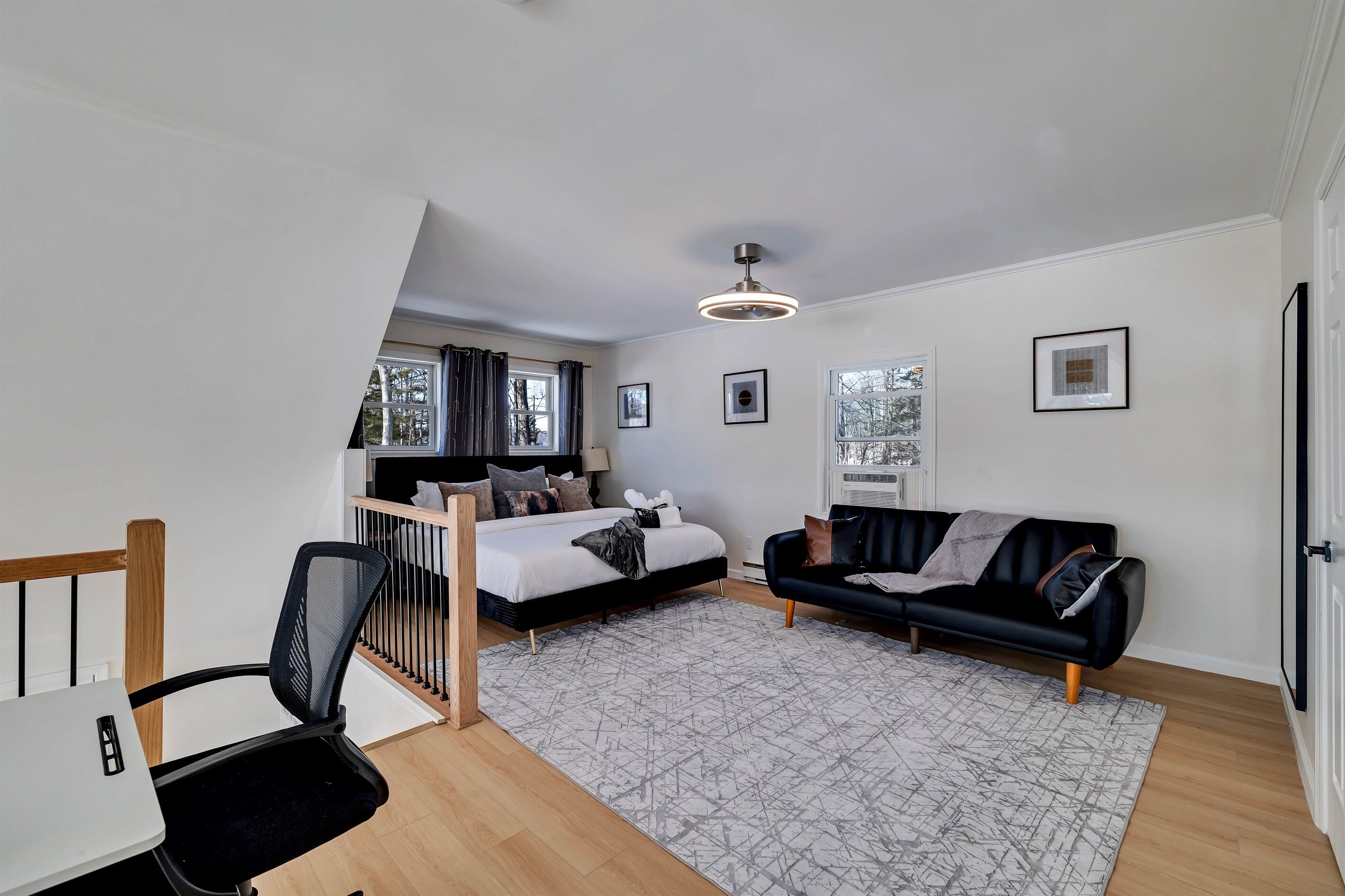 Ein modernes Schlafzimmer mit einem Bett, einer schwarzen Couch, einem Schreibtisch und einer Treppe zu einer oberen Ebene.