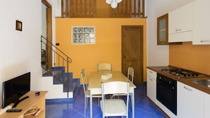 A compact kitchen with a dining table, chairs, a TV, and a staircase leading to an upper level. - Visitsicilia Le Magnolie 1 (Castellammare del Golfo)