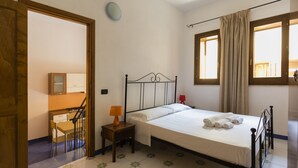 A bedroom with a bed, a nightstand, a lamp, a chair, a desk, a mirror, and a window with curtains. - Visitsicilia Le Magnolie 1 (Castellammare del Golfo)