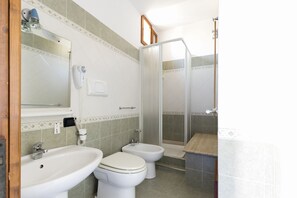 Un baño con lavamanos, dos inodoros, un bidé, un espejo y una cabina de ducha.