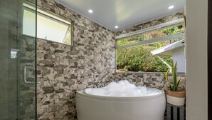 A modern bathroom with a stone wall, a glass shower enclosure, and a large white bathtub. - House of Turri: Suite | Views | Terrace | Jacuzzi (Turrialba)