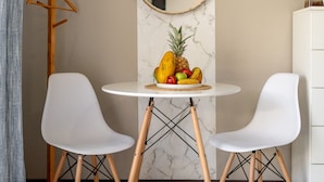 A dining area with a round table, two white chairs, a fruit bowl, a hanging mirror, and a coat rack. - House of Turri: Suite | Views | Terrace | Jacuzzi (Turrialba)