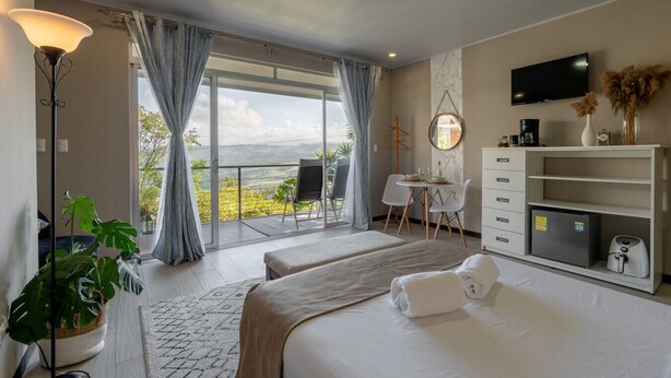 A hotel room with two beds, a desk, a chair, a TV, and a view of the outdoors. - House of Turri: Suite | Views | Terrace | Jacuzzi (Turrialba)