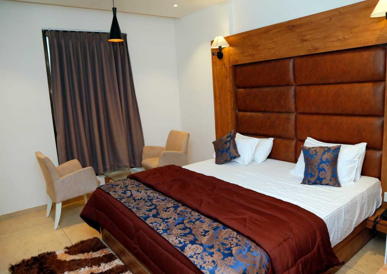 Una camera d'albergo con un letto grande, una testiera in legno, una scrivania, una sedia e una finestra con tende.