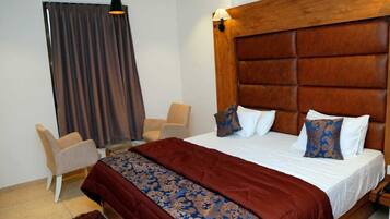 Una camera d'albergo con un letto grande, una testiera in legno, una scrivania, una sedia e una finestra con tende.
