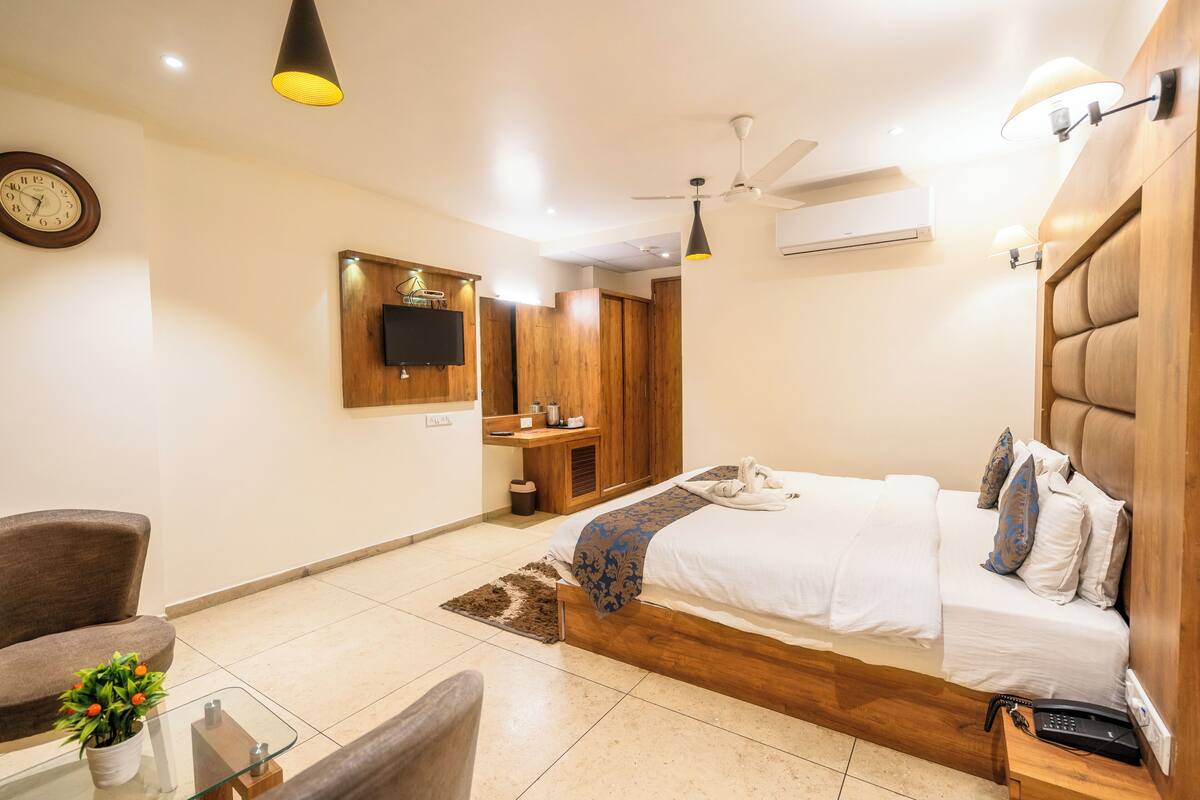 A modern hotel room with a wooden bed, a desk, a chair, a clock, and a television on the wall.