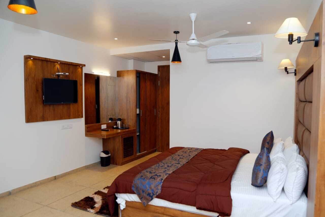 A bedroom with a bed, a TV mounted on the wall, a wardrobe, a ceiling fan, and a light fixture.