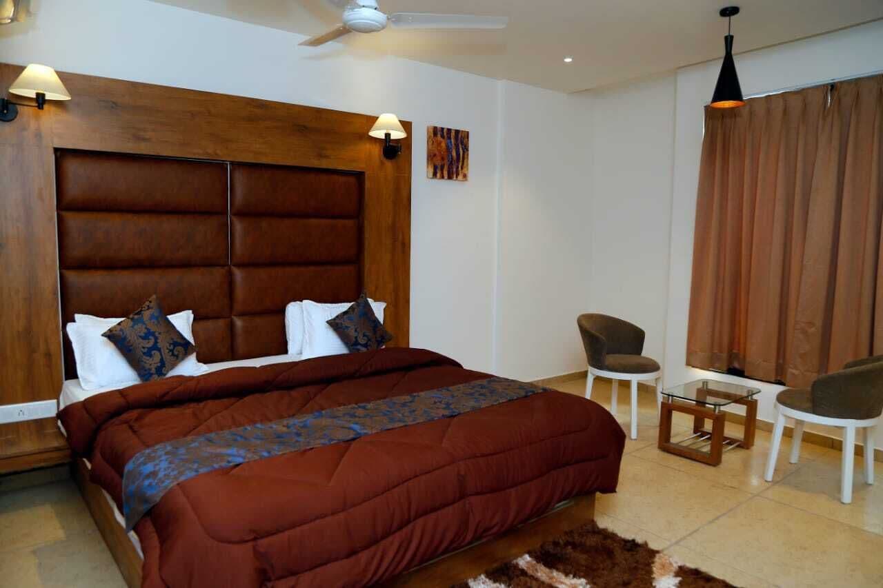 Un dormitorio con una cama grande, cabecera de madera, dos lámparas de noche, una mesita, dos sillas y un ventilador de techo.