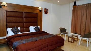 Un dormitorio con una cama grande, cabecera de madera, dos lámparas de noche, una mesita, dos sillas y un ventilador de techo.