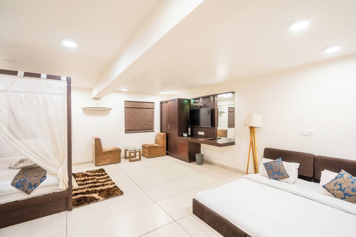 A modern hotel room with a bed, a sofa, a TV, and a small seating area.