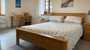 Een slaapkamer met een houten bed, een bureau, een stoel, een nachtkastje en een raam met gordijnen.
