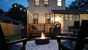 Un patio trasero con un brasero, asientos al aire libre y luces colgantes.