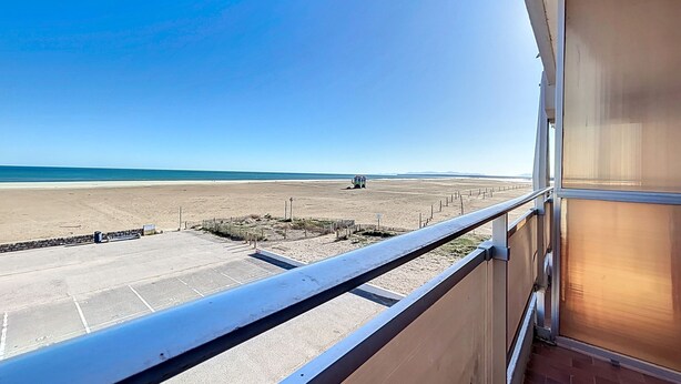 A balcony with a view of a beach and a distant vehicle.