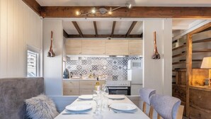 Een eetgedeelte met een witte tafel voor vier personen, een houten plafond en een keuken op de achtergrond met decoratieve tegels.