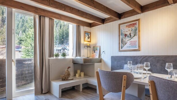 Een eethoek met een houten plafond, een bank en een tafel voor twee compleet met glazen en bestek.