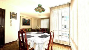 A dining area with a round table covered in a lace tablecloth, surrounded by wooden chairs.