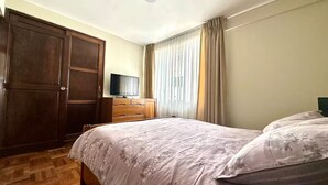 A bedroom with a bed, a TV, a wardrobe, and a window with curtains.