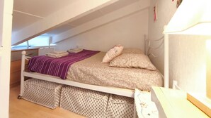 Une petite chambre de style loft, aux murs blancs, comprenant un lit, des oreillers et une table de chevet.