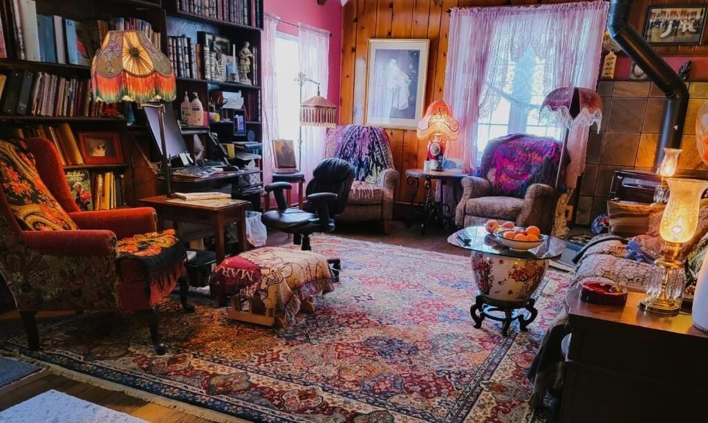 A cozy living room with a large bookshelf, a patterned rug, and a variety of seating options.