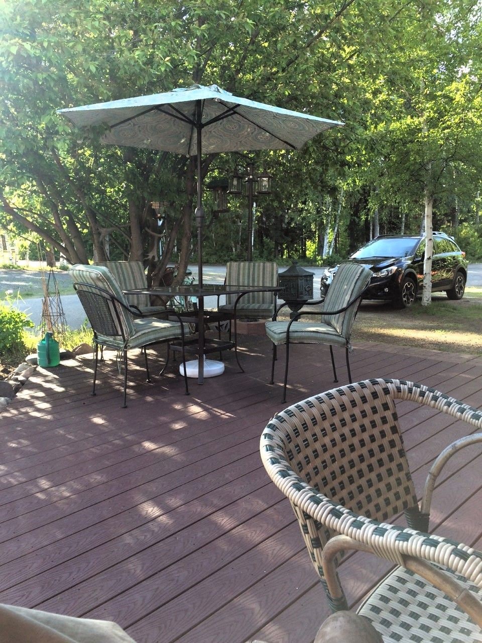 An outdoor patio with a table and chairs, a covered umbrella, and a car parked nearby.