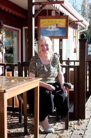 A woman seated at a wooden table outside a building with a sign reading "Bella's Backpacker Hotel." - Billie's Backpackers Hostel (Fairbanks)