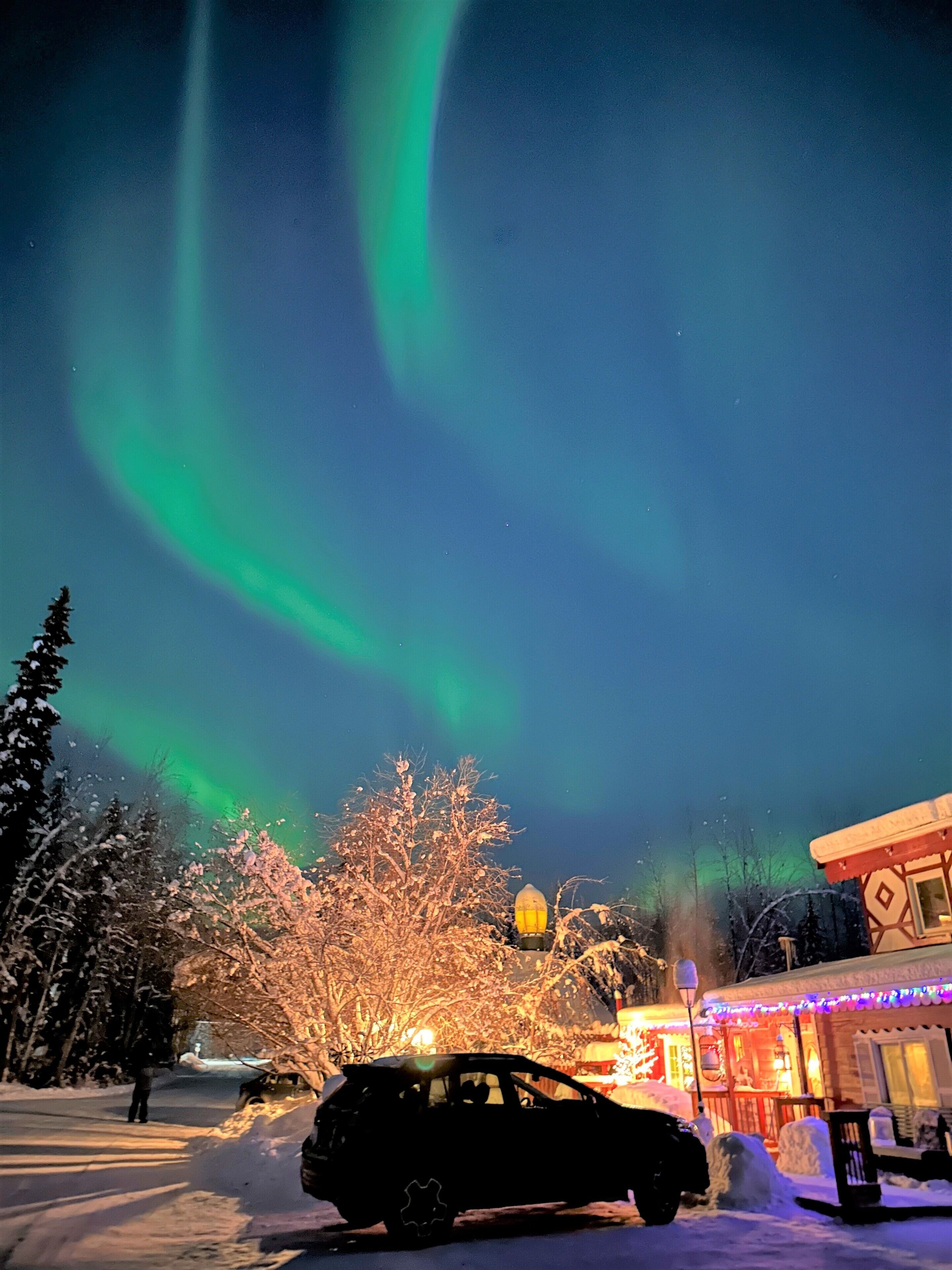 A car parked in a snowy area with a house and trees in the background.