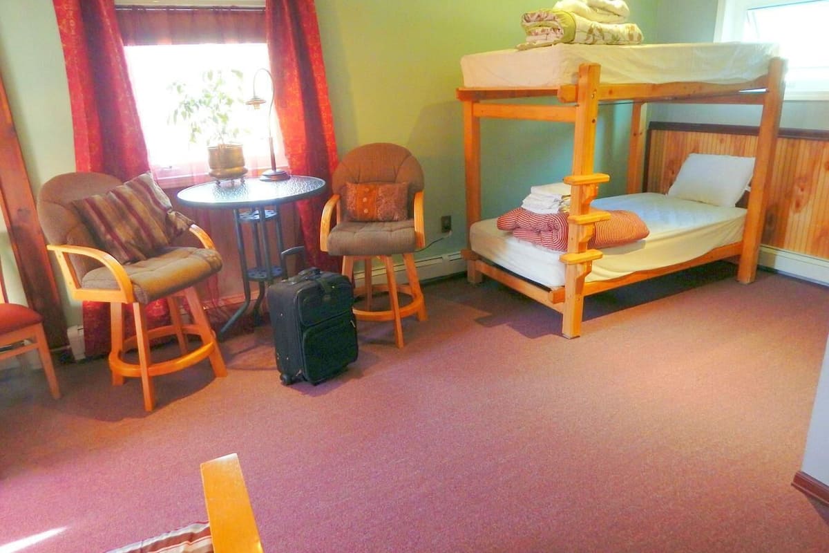 A bunk bed with a small table and two chairs in a room with a carpeted floor.