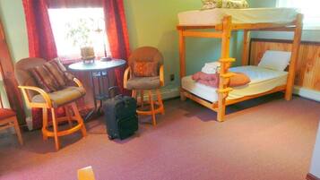 Una cama litera con una mesita pequeña y dos sillas en una habitación con piso alfombrado.