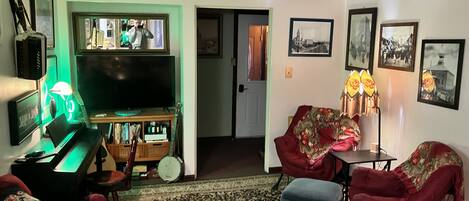 Una sala de estar con televisor, piano y un sillón rojo.