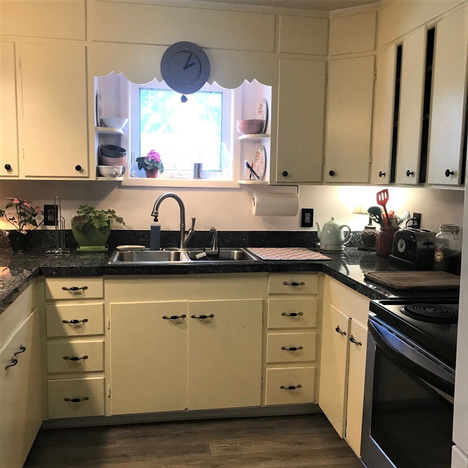 A kitchen with white cabinets, a black countertop, a sink, and a clock above the window.