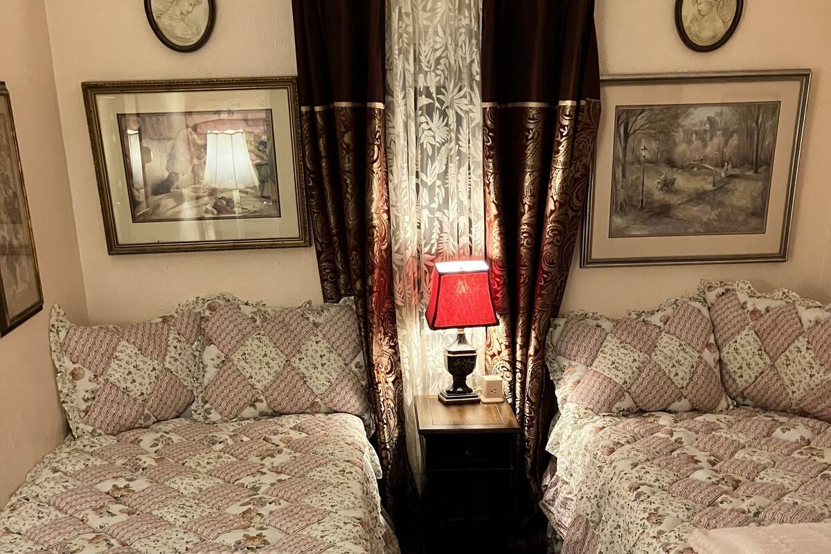 A room with two beds, a nightstand with a lamp, and curtains.