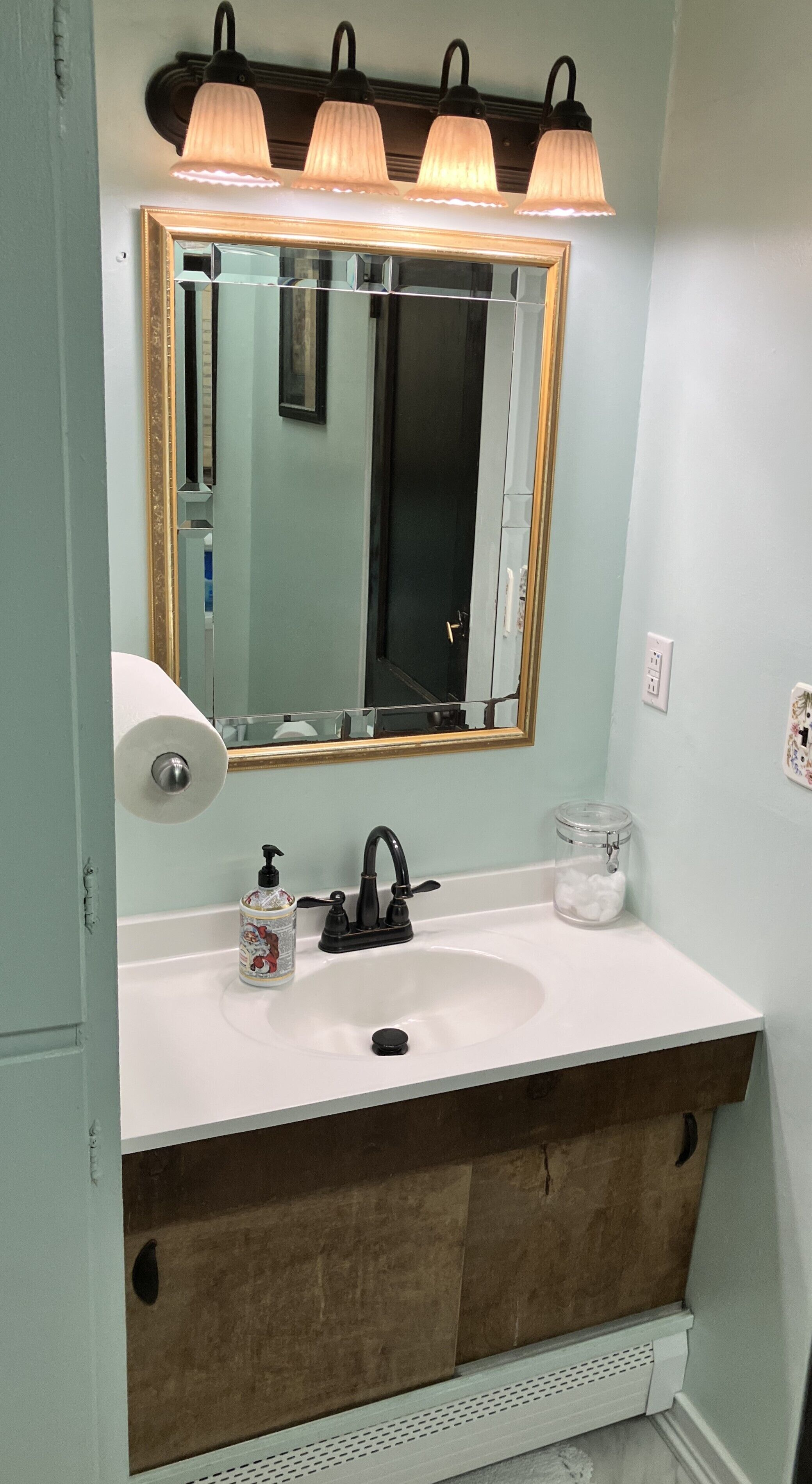 A bathroom with a white sink, a mirror with a gold frame, and three wall-mounted lights.