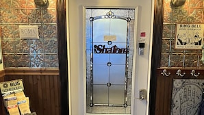 L'ingresso di un hotel con una porta decorativa, un cartello con la scritta "Roma" e un pannello orari degli autobus.