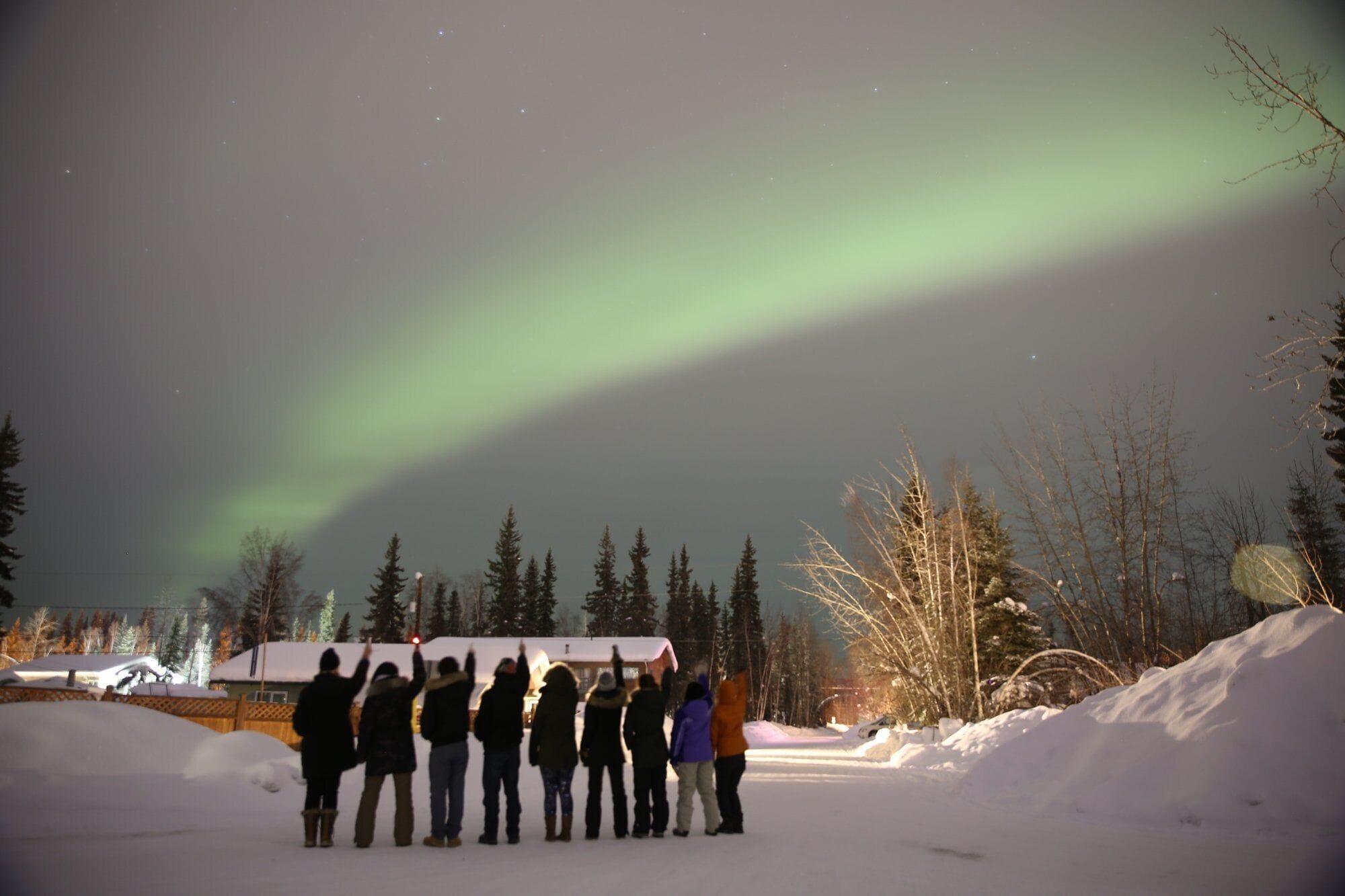 A group of people standing in a snowy outdoor area with a house in the background.