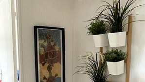A hallway with a framed painting, a wooden ladder shelf with potted plants, and a woven light fixture. - Nice house with garden near the beach (Dives-sur-Mer)