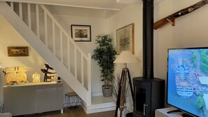 A living room with a staircase, a black wood-burning stove, a television, and a cabinet with decorative items. - Nice house with garden near the beach (Dives-sur-Mer)